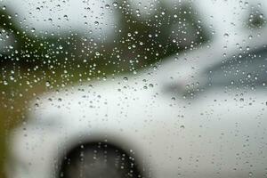 gotas de lluvia en coche ventanas noche después trabajo en el estacionamiento, de cerca fotografía, antecedentes con blanco carros borroso y el imagen es horizontal y hermosa. foto