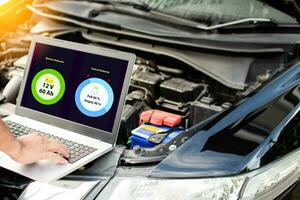 Closeup, man's hand typing on laptop computer keyboard to check the operation of the car engine in the garage. The engine of a car does not start. Notebook computer screen shows battery and oil status photo