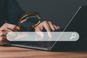 Hand of businessman holding of magnifying glass, working with computer laptop in office. Searching Browser Internet Data Information with search job. Search Engine Optimization SEO Networking Concept. photo