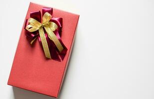 The red color Presents celebrate box with red and gold ribbons placed on a white table with copy space on the right can input text, take close-up photography, and top view, image is landscape. photo