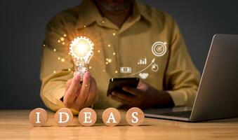 businessman hand holding a light bulb on wood block with text ideas for business corporate, new idea concept with innovation and inspiration, innovative technology in science and communication concept photo
