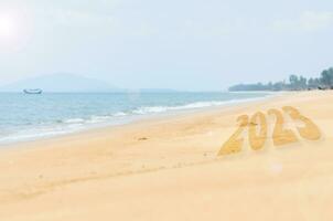 New Year 2023 Concept. inscription is a 2023 number on sand beach. Sandy beach and sea wave beautiful background. Write letters by hand on the beach. change new year of 2023 on sand of beach photo