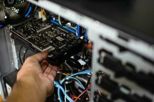 A technician hand holds the graphics card to fix it. The VGA card is damaged causing the computer to fail. Display card does not display a personal computer screen. Take closeup photo. Blur background photo