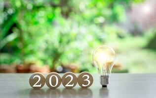 el nuevo año 2023 y brillante ligero bulbo en mesa. concepto de un puesta en marcha ese unidades economía, finanzas, bancario, adelante, futuro, brillante, puesta en marcha de negocio en 2023, estrategia, éxito. bokeh antecedentes foto