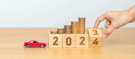 2023 flipping to 2024 year block with car model and Coins Money stack for deposit and Automobile Tax. Money Saving, Car Insurance, Financial, vehicle Repair and Maintenance and New Year concept photo