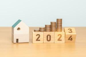 2023 flipping to 2024 year block with house model and Coins stack. real estate, Home loan, tax, investment, mortgage, financial, savings and New Year Resolution concepts photo
