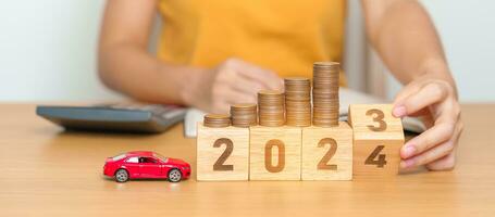 2023 flipping to 2024 year block with car model and Coins Money stack for deposit and Automobile Tax. Money Saving, Car Insurance, Financial, vehicle Repair and Maintenance and New Year concept photo