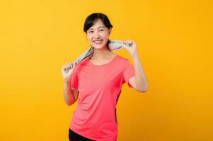 Portrait young asian sports fitness woman happy smile wearing pink sportswear and face towel doing exercise training workout against yellow studio background. wellbeing and healthy lifestyle concept. photo