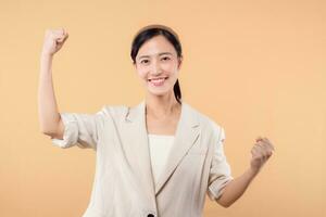 Studio portrait of happy successful confident young asian business woman. Beautiful young lady in white jacket smiling at camera standing isolated on solid beige colour copyspace background photo