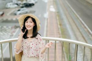 young asian woman traveler with weaving basket using mobile phone and standing on overpass with railway background. Journey trip lifestyle, world travel explorer or Asia summer tourism concept. photo