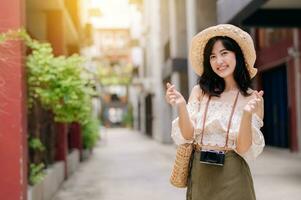 Happy youth asian woman with camera travels street city trip on leisure weekend. Young hipster female tourist sightseeing summer urban Bangkok destination. Asia summer tourism concept. photo