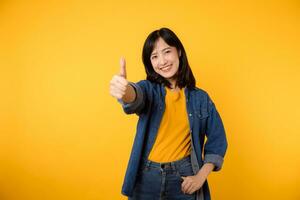 Portrait young happy asian woman cheerful smile showing thumb up, trust, recommend gesture isolated on yellow studio background. Pretty attractive female with like hand sign. lifestyle girl woman photo