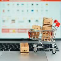 cajas con compras carro en un ordenador portátil computadora. en línea compras, mercado plataforma sitio web, tecnología, comercio electrónico, Envío entrega, logística y en línea pago conceptos foto