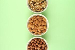 Almond, hazelnut, walnut on white ceramic bowl on green background. Healthy eating diet, nutrition, vegan concept. Protein organic food. Dry snack. National nut day. Copy space for text photo