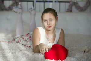 Very beautiful teen girl lying on a bed with a red heart pillow.Young lady photo