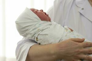The doctor's hands hold a newborn baby wrapped in a diaper. photo