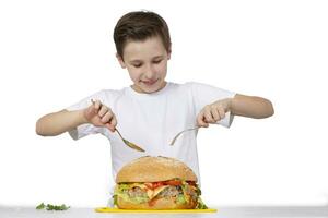 joven chico con grande hamburguesa aislado en blanco. un adolescente sostiene un dorado tenedor y un cuchara. foto