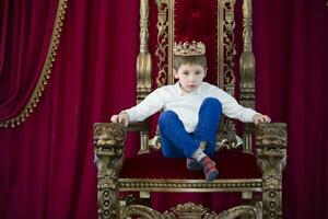 pequeño chico en un corona en un lujoso silla foto