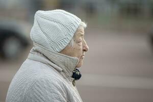 el cara de un mayor mujer en un perfil en calentar ropa. un triste pensionista en gris ropa. foto