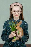 Funny girl in glasses feeds a red rabbit with parsley. photo