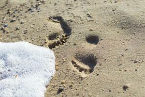 Footprints in the sand and foam from the wave photo