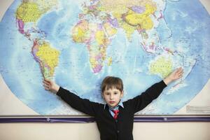 The child stands at the geographical map of the world. Elementary school student smiles at the map of the world. photo