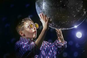 A young boy in glasses touches a disco ball with his hands. Children's disco, party. photo