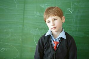 Sad Student child in class. Schoolboy at the green blackboard with a boring face. Education problems in primary grades.Didn't learn the lesson photo