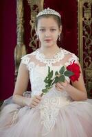 Teenager girl smart in red luxury royal armchair. Girl princess.Queen in a red chair.Luxurious young lady with a scarlet rose in a white dress in an old red armchair photo