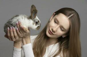 Happy young girl holding a white rabbit on a gray background photo