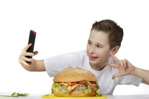 A young boy takes a selfie with a big hamburger, isolated in white. photo