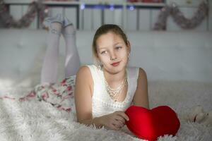 muy hermosa adolescente niña acostado en un cama con un rojo corazón almohada. foto