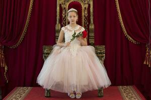 Teenager girl smart in red luxury royal armchair. Girl princess.Queen in a red chair.Luxurious young lady with a scarlet rose in a white dress in an old red armchair photo