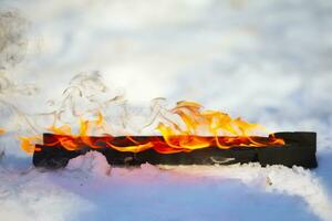 Burning log in the snow. Fire on a wooden stick. photo