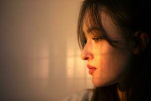 The face of a pensive girl in profile is illuminated by warm light from the window. photo