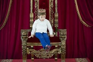 pequeño chico en un corona en un lujoso silla foto