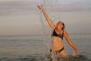 Woman in sea water with splashes. Female tanned figure jumps out of the sea photo