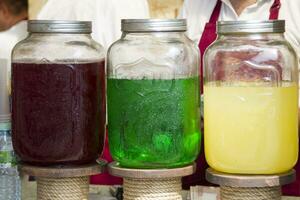 Glass jars with multi-colored lemonade. Bright summer drinks with fruits and herbs photo