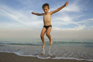 el niño saltos fuera de el agua. el chico saltos en el océano. vacaciones a el playa foto