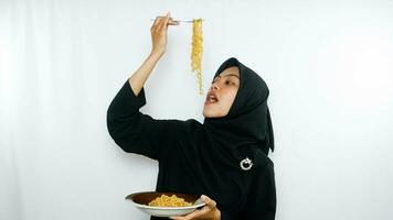 Young asian woman isolated on white background holding a plate of noodles with fork and eating it photo