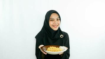 Young asian woman isolated on white background holding a plate of noodles with fork and eating it photo