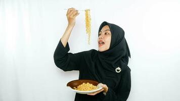 Young asian woman isolated on white background holding a plate of noodles with fork and eating it photo
