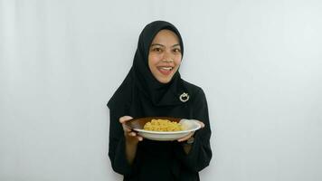 Young asian woman isolated on white background holding a plate of noodles with fork and eating it photo