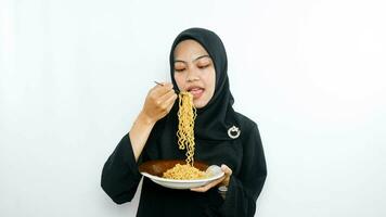 Young asian woman isolated on white background holding a plate of noodles with fork and eating it photo