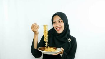 Young asian woman isolated on white background holding a plate of noodles with fork and eating it photo