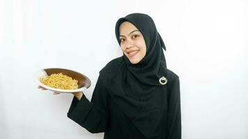 Young asian woman isolated on white background holding a plate of noodles with fork and eating it photo