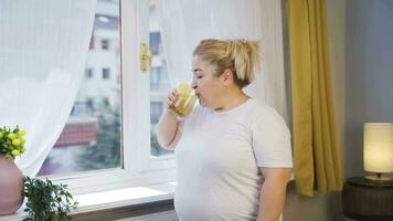 Obesity woman drinking diet beverage in front of window. video