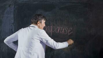 Male doctor writes Menopause on the blackboard. video