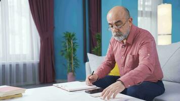 vieux homme à la recherche à factures calculateur avec calculatrice à maison. video