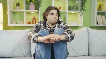 Depressed and worried young man sitting alone on sofa at home. video